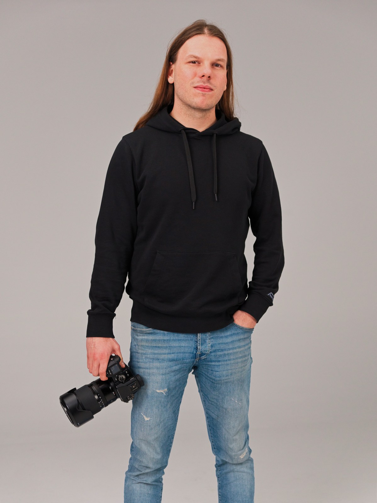 Luka Radojević holding a camera, wearing a black hoodie and blue jeans.