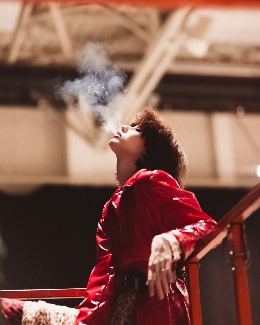 Fashion portrait of a person in a red coat exhaling smoke.