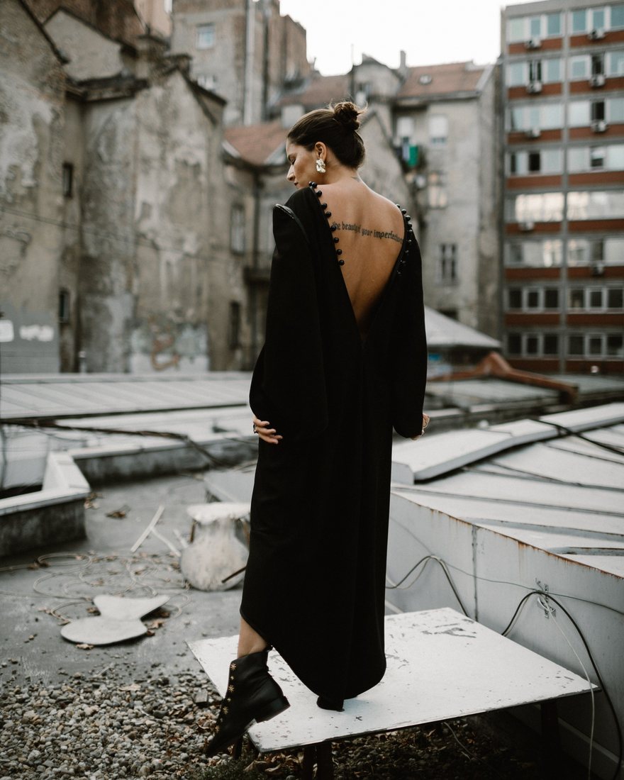 Fashion portrait of a woman in a long black dress on a rooftop.