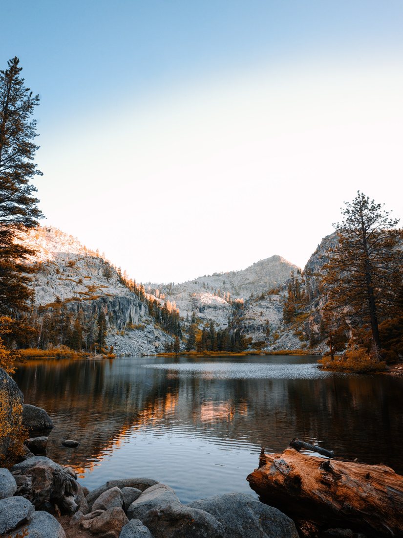 A mountain lake with pine trees, rocky peaks, and reflections in the water.