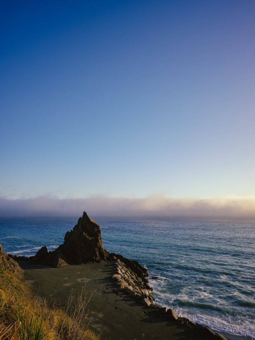 A rocky coastal outcrop overlooks the ocean beneath a blue sky.