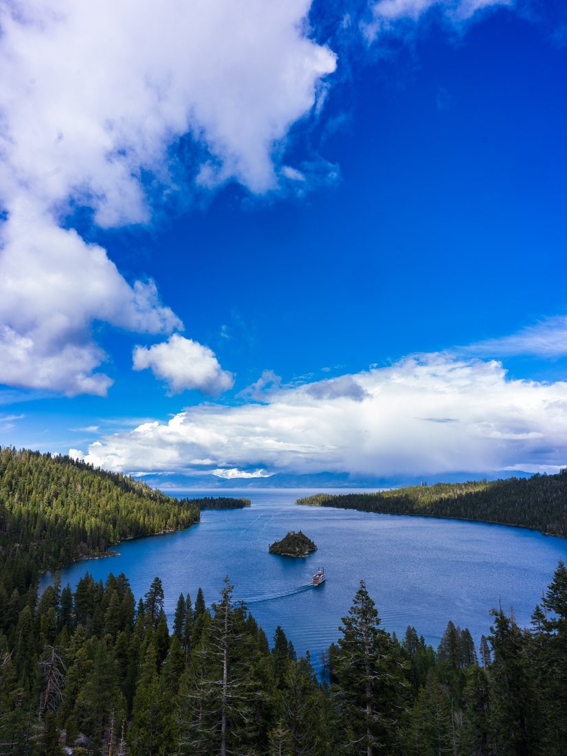 A lake with a small island lies between forested slopes beneath a blue sky.