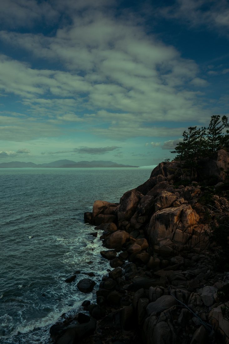 Waves meet a rocky shore beneath a cloudy evening sky.