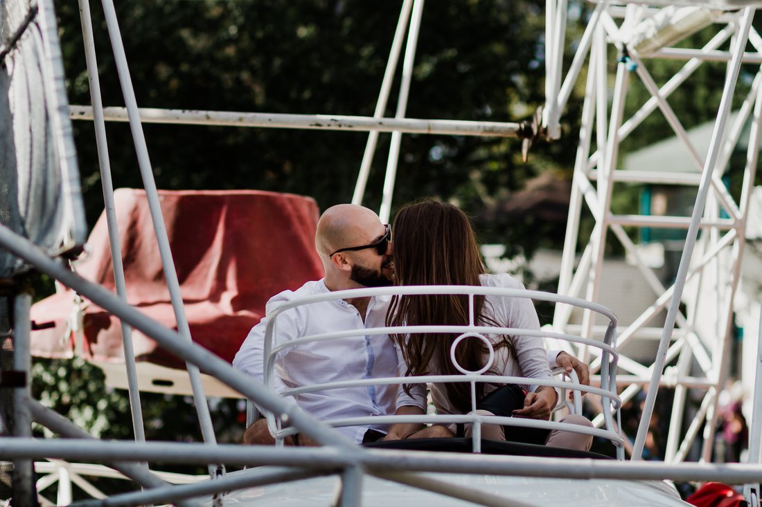 A couple share a kiss while seated together on a Ferris wheel.